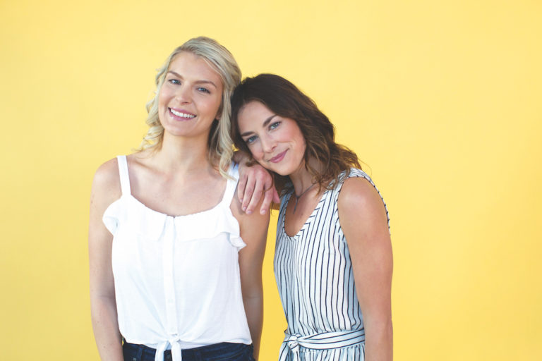 two female friends smiling in front of yellow backdrop