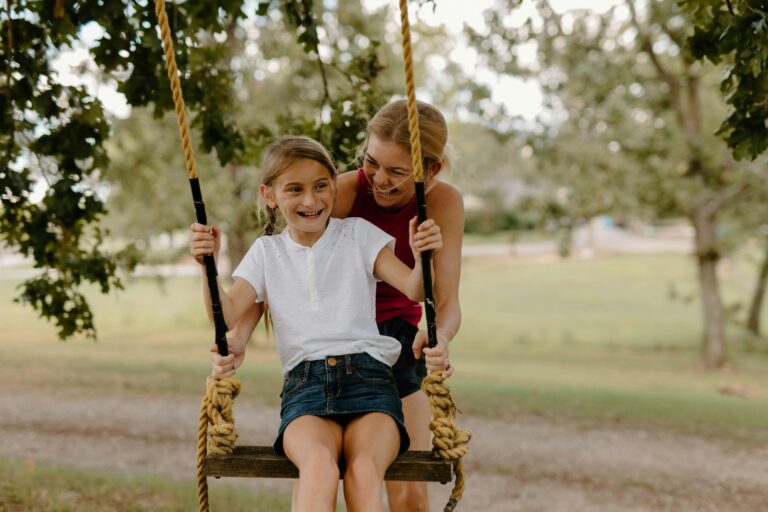A mom happily pushes her daughter on a tree swing
