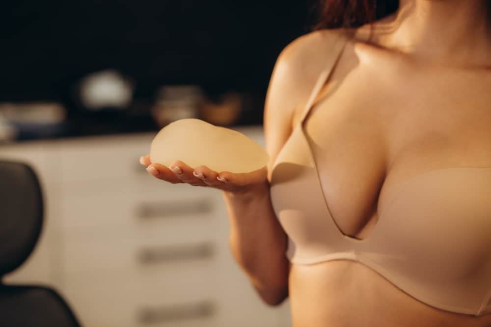 A cropped shot of a woman in a beige bra holding a breast implant